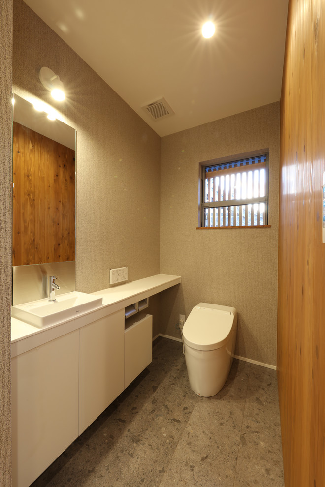 Small plywood floor and gray floor powder room photo in Other with white cabinets, beige walls, a vessel sink, solid surface countertops, white countertops and a one-piece toilet