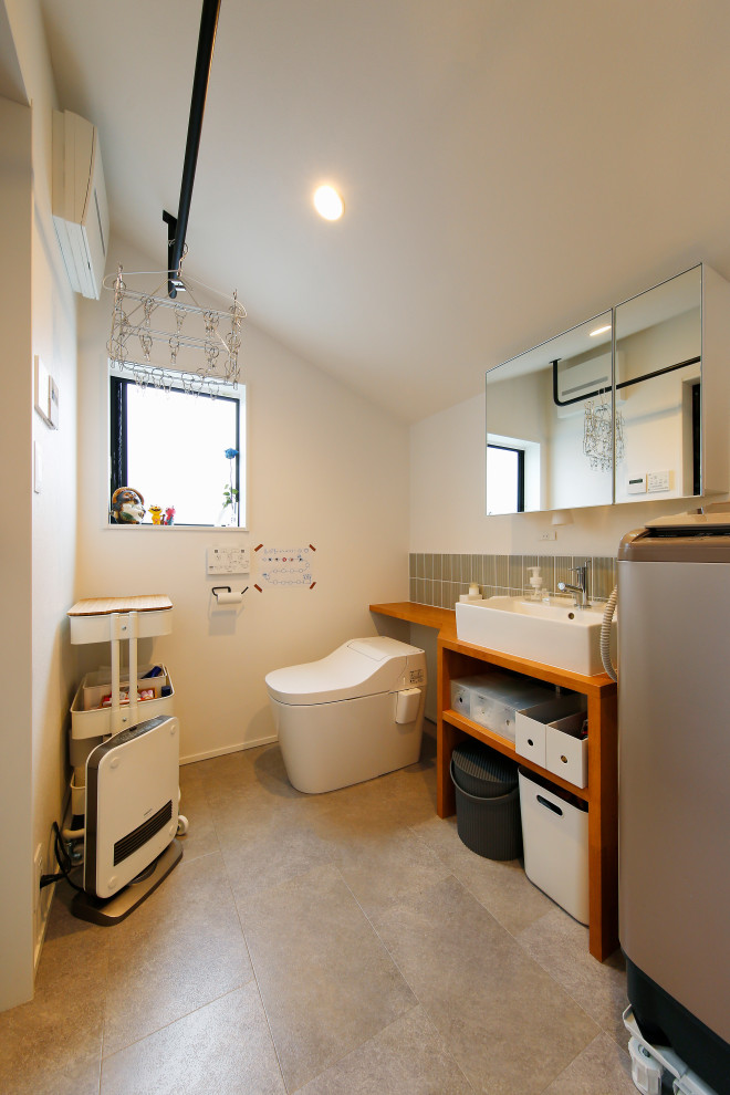 東京都下にあるお手頃価格の中くらいなインダストリアルスタイルのおしゃれなトイレ・洗面所 (オープンシェルフ、茶色いキャビネット、分離型トイレ、グレーのタイル、セラミックタイル、白い壁、テラゾーの床、アンダーカウンター洗面器、木製洗面台、ベージュの床、ブラウンの洗面カウンター、造り付け洗面台、クロスの天井、壁紙) の写真