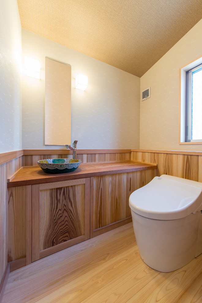 Mittelgroße Asiatische Gästetoilette mit beiger Wandfarbe, hellem Holzboden, Waschtischkonsole, Waschtisch aus Holz, beigem Boden und brauner Waschtischplatte in Sonstige