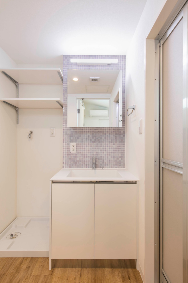 東京23区にある低価格の中くらいな北欧スタイルのおしゃれなトイレ・洗面所 (インセット扉のキャビネット、白いキャビネット、一体型トイレ	、マルチカラーのタイル、モザイクタイル、紫の壁、淡色無垢フローリング、アンダーカウンター洗面器、人工大理石カウンター、ベージュの床、白い洗面カウンター、造り付け洗面台、クロスの天井、レンガ壁) の写真