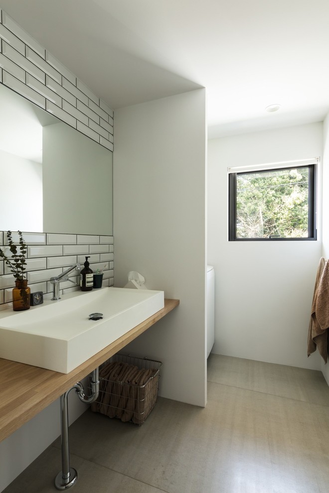 大阪にある中くらいなインダストリアルスタイルのおしゃれなトイレ・洗面所 (白いタイル、サブウェイタイル、白い壁、セメントタイルの床、オーバーカウンターシンク、木製洗面台、グレーの床、ブラウンの洗面カウンター) の写真