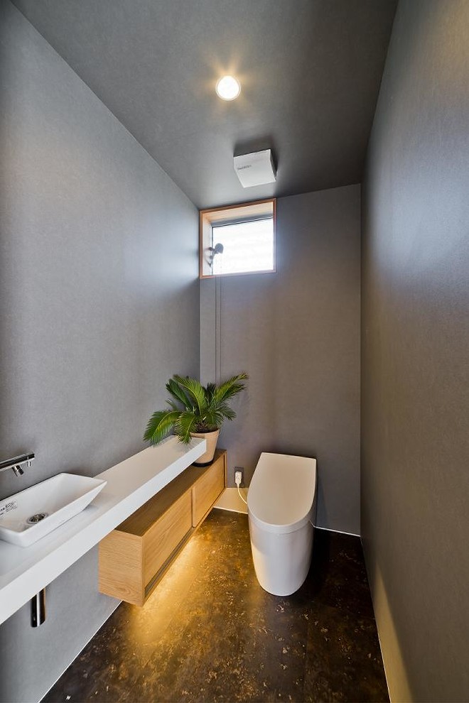 Réalisation d'un WC et toilettes asiatique avec un mur gris, une vasque, un sol noir et un plan de toilette blanc.