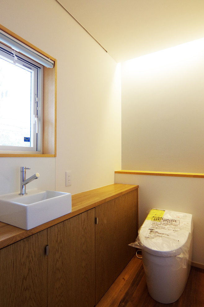 На фото: туалет среднего размера в скандинавском стиле с унитазом-моноблоком, белыми стенами, паркетным полом среднего тона, накладной раковиной, столешницей из дерева, коричневым полом и белой столешницей