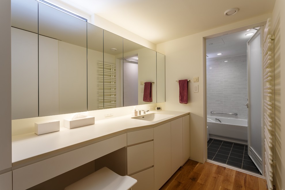 Mittelgroße Moderne Gästetoilette mit flächenbündigen Schrankfronten, weißen Schränken, weißer Wandfarbe, braunem Holzboden, integriertem Waschbecken und braunem Boden in Sonstige
