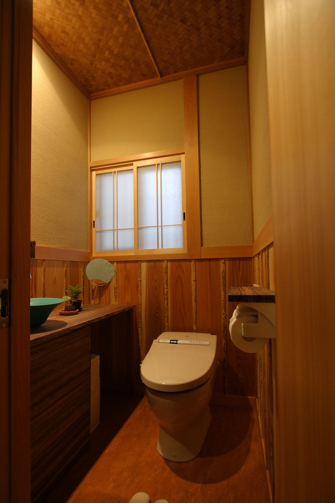 Idéer för små orientaliska brunt toaletter, med släta luckor, skåp i mörkt trä, bruna väggar, ett fristående handfat, träbänkskiva, brunt golv, en toalettstol med hel cisternkåpa och linoleumgolv