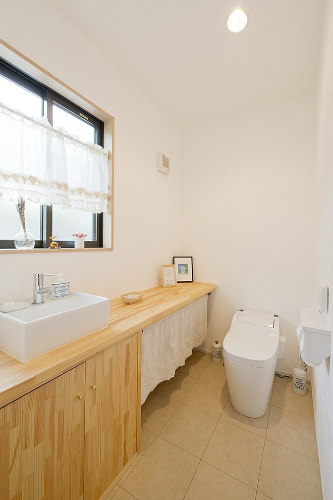 Cette image montre un WC et toilettes rustique en bois clair avec un placard à porte plane, un mur blanc, une vasque, un plan de toilette en bois, un sol beige et un plan de toilette beige.
