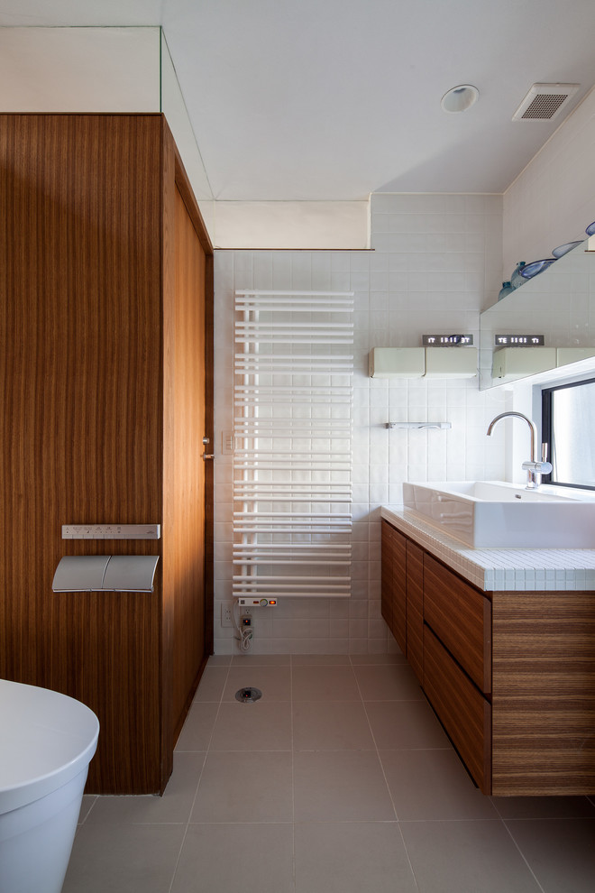 Foto di un bagno di servizio moderno con ante in legno scuro, pareti bianche, lavabo a bacinella, top piastrellato e pavimento grigio