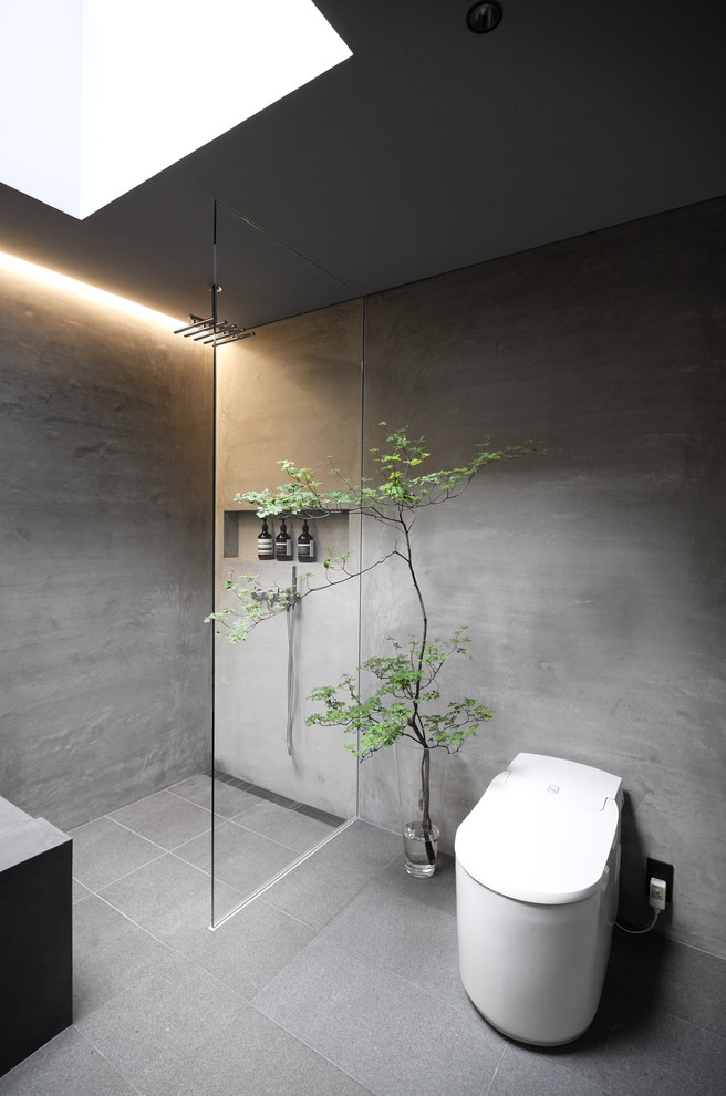 Inredning av ett industriellt litet grå grått toalett, med en toalettstol med hel cisternkåpa, grå kakel, grå väggar, skiffergolv, ett integrerad handfat, bänkskiva i betong och grått golv