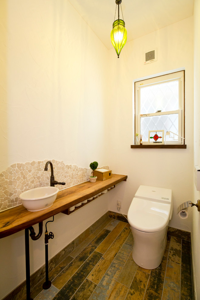 Exemple d'un WC et toilettes méditerranéen en bois foncé avec un placard sans porte, WC à poser, un carrelage multicolore, des carreaux de porcelaine, un mur blanc, sol en stratifié, une vasque, un plan de toilette en bois, un sol multicolore et un plan de toilette marron.