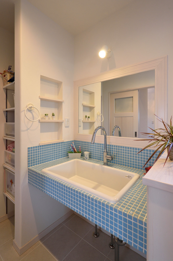 他の地域にある北欧スタイルのおしゃれなトイレ・洗面所 (白い壁、オーバーカウンターシンク、タイルの洗面台、グレーの床、青い洗面カウンター) の写真