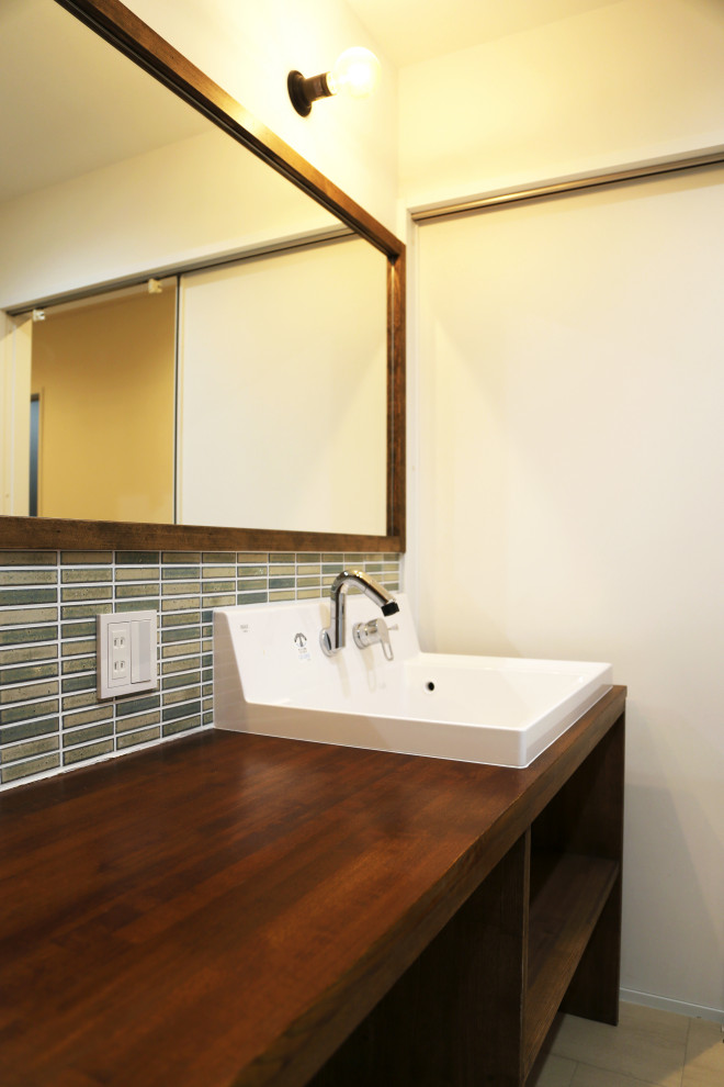 Cette photo montre un WC et toilettes moderne en bois foncé avec un placard sans porte, un carrelage vert, un mur blanc, un plan de toilette marron et meuble-lavabo encastré.