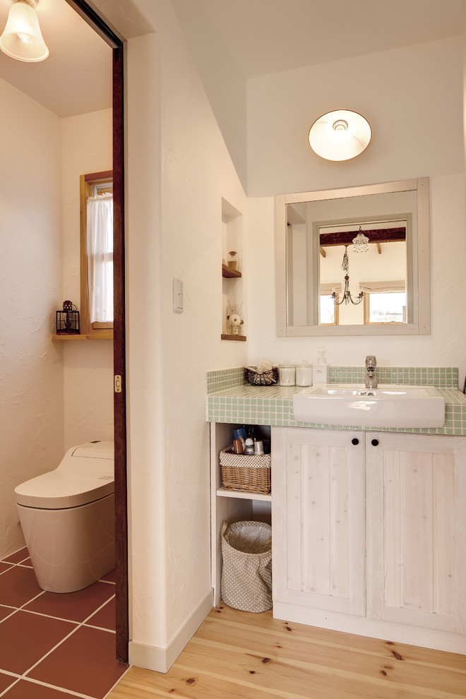 Bild på ett lantligt toalett, med luckor med infälld panel, vita väggar, ljust trägolv och brunt golv