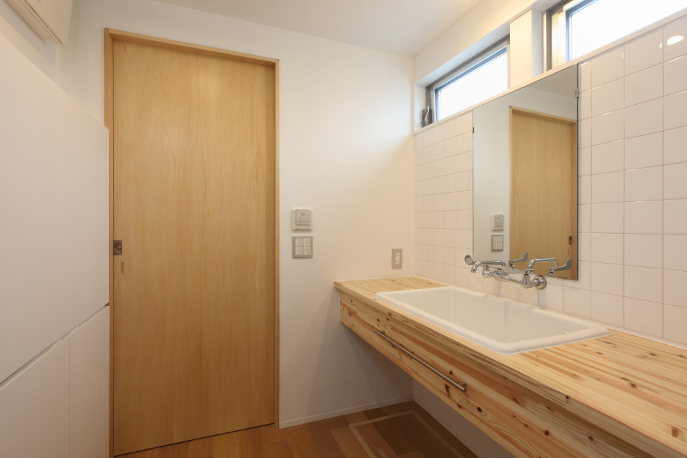 Aménagement d'un WC et toilettes moderne en bois brun de taille moyenne avec un placard sans porte, un carrelage blanc, des carreaux de porcelaine, un mur blanc, un sol en bois brun, un lavabo encastré, un plan de toilette en bois, un sol marron et un plan de toilette marron.