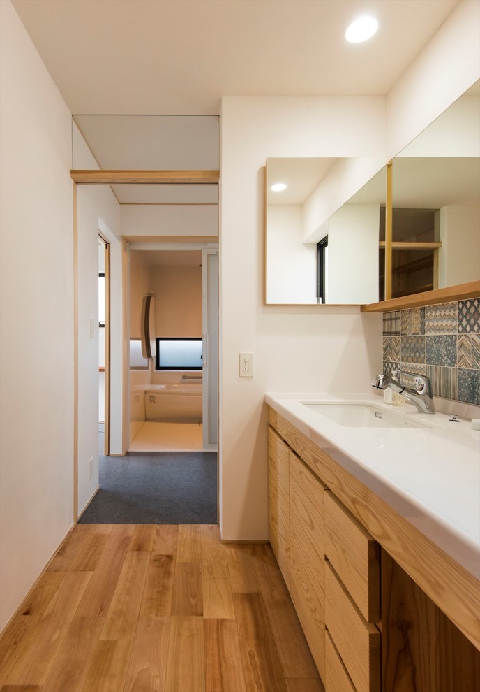 На фото: туалет в современном стиле с фасадами цвета дерева среднего тона, синей плиткой, белыми стенами, паркетным полом среднего тона, врезной раковиной, коричневым полом и белой столешницей