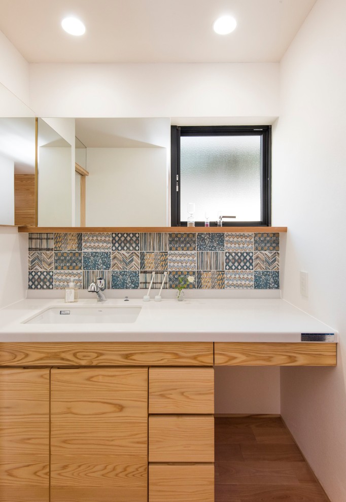 Immagine di un bagno di servizio minimalista con ante in legno scuro, piastrelle blu, pareti bianche, pavimento in legno massello medio, lavabo sottopiano, pavimento marrone e top bianco