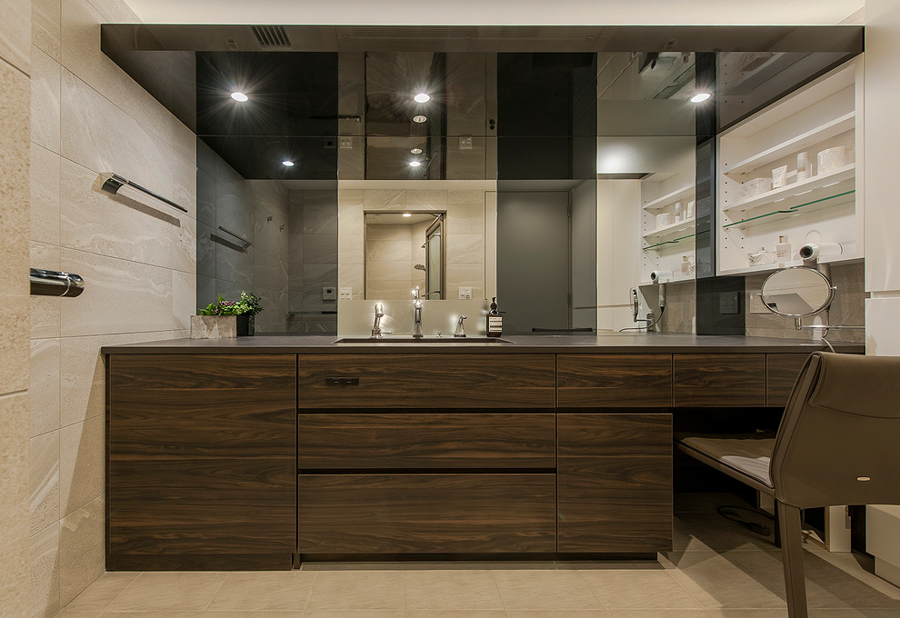 Moderne Gästetoilette mit dunklen Holzschränken, beigen Fliesen, beiger Wandfarbe, Unterbauwaschbecken, beigem Boden und schwarzer Waschtischplatte