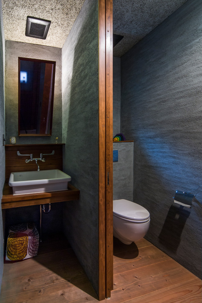 На фото: туалет в стиле рустика с серыми стенами, паркетным полом среднего тона, настольной раковиной, столешницей из дерева, инсталляцией и коричневой столешницей