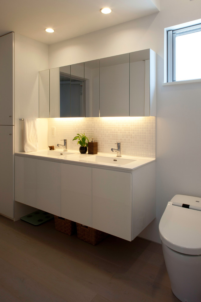 Idéer för ett mellanstort modernt vit toalett, med luckor med profilerade fronter, vita skåp, en toalettstol med hel cisternkåpa, vit kakel, mosaik, vita väggar, plywoodgolv, ett undermonterad handfat, bänkskiva i akrylsten och beiget golv