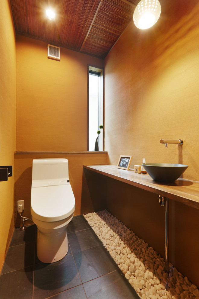 Diseño de aseo asiático con paredes marrones, lavabo sobreencimera y suelo negro