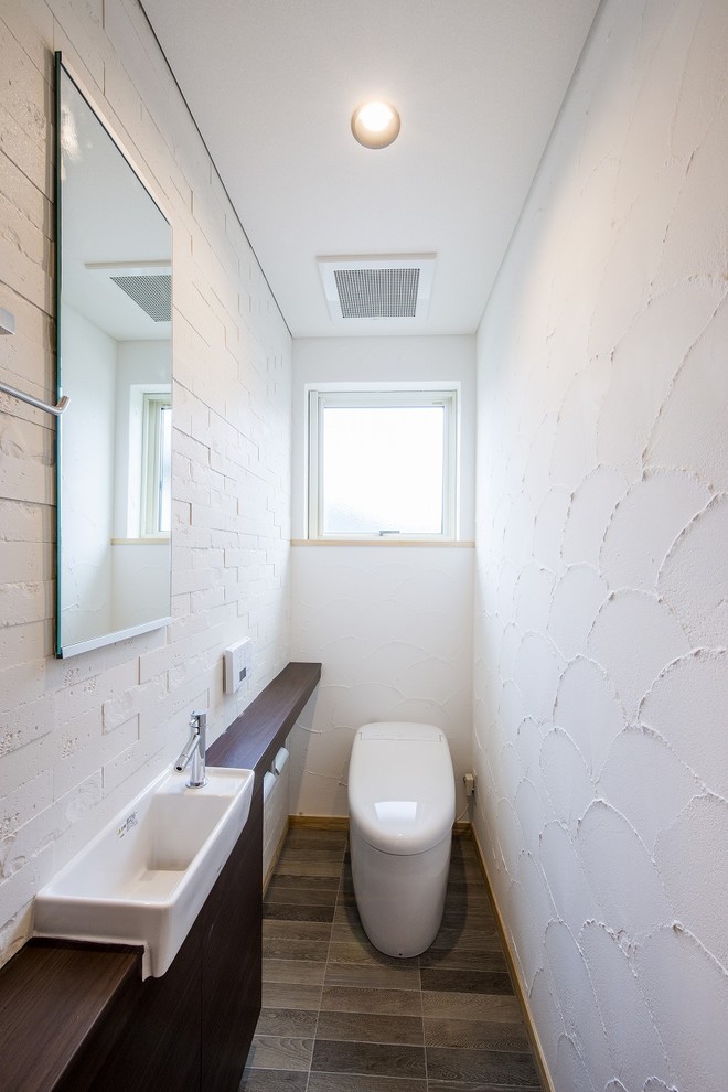 Exempel på ett modernt brun brunt toalett, med vita väggar, ett nedsänkt handfat, träbänkskiva och grått golv