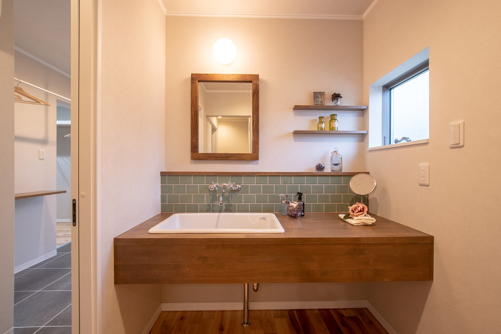 Foto på ett litet lantligt brun toalett, med vita väggar, mellanmörkt trägolv, ett nedsänkt handfat, brunt golv, grön kakel och träbänkskiva