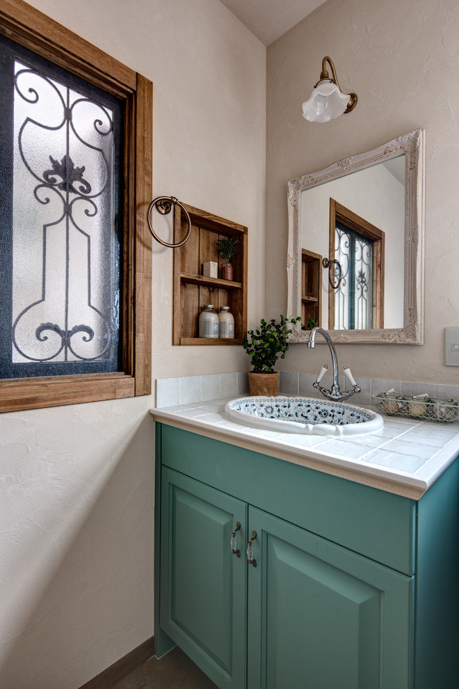 Пример оригинального дизайна: туалет в классическом стиле с фасадами с утопленной филенкой, зелеными фасадами, бежевыми стенами, накладной раковиной и столешницей из плитки