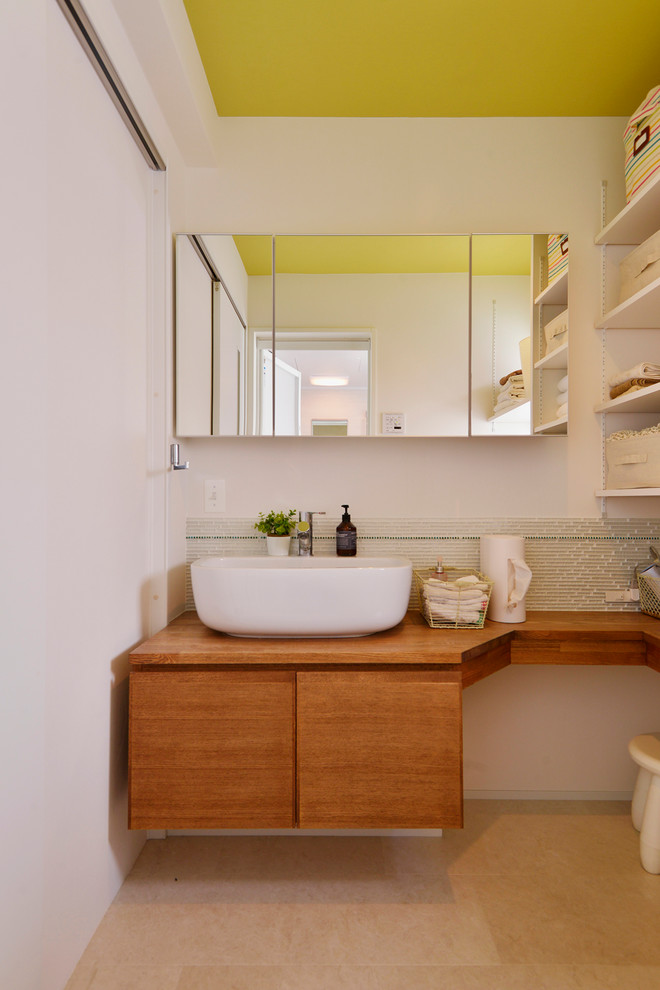 Modern inredning av ett toalett, med släta luckor, skåp i mellenmörkt trä, vita väggar, ett fristående handfat och beiget golv