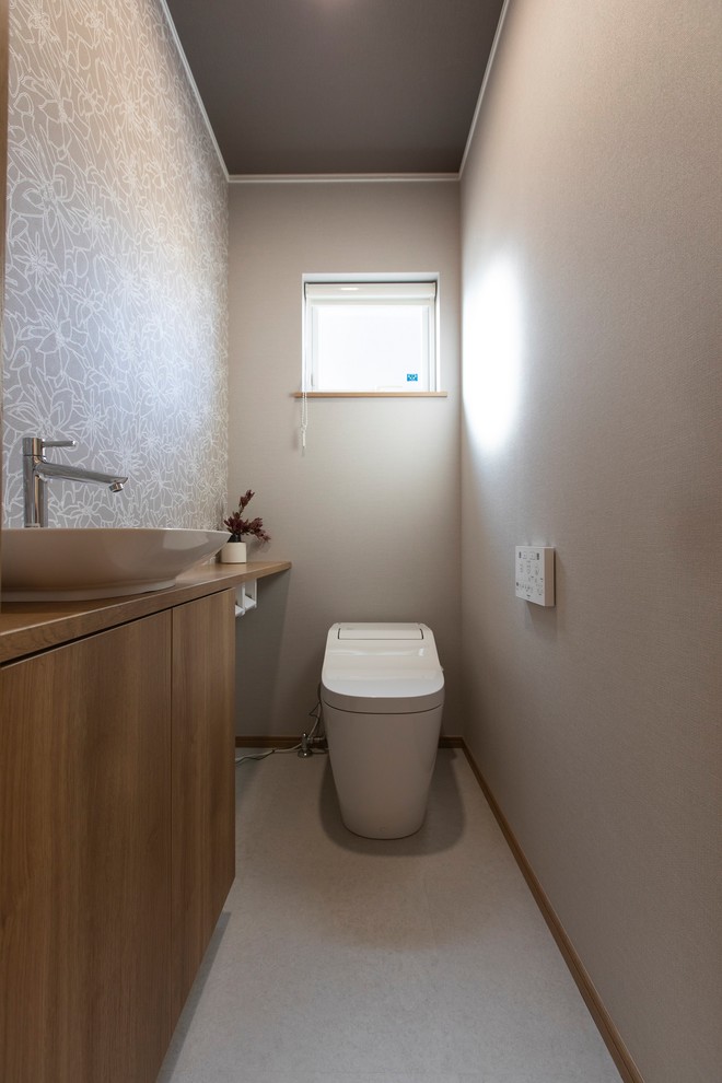 Idée de décoration pour un WC et toilettes minimaliste en bois brun de taille moyenne avec un placard à porte plane, un mur gris, une vasque, un plan de toilette en bois, un sol gris et un plan de toilette marron.