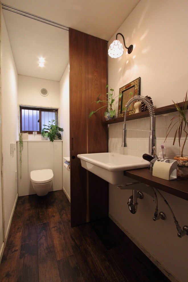 Cette photo montre un WC et toilettes chic avec un placard à porte plane, des portes de placard blanches, WC séparés, un carrelage blanc, des carreaux de porcelaine, un mur blanc, un sol en vinyl, une grande vasque, un plan de toilette en bois et un sol marron.
