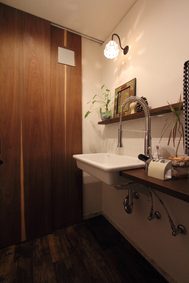 Exemple d'un WC et toilettes chic avec WC séparés, un carrelage blanc, des carreaux de porcelaine, un mur blanc, un sol en vinyl, une grande vasque, un plan de toilette en bois et un sol marron.
