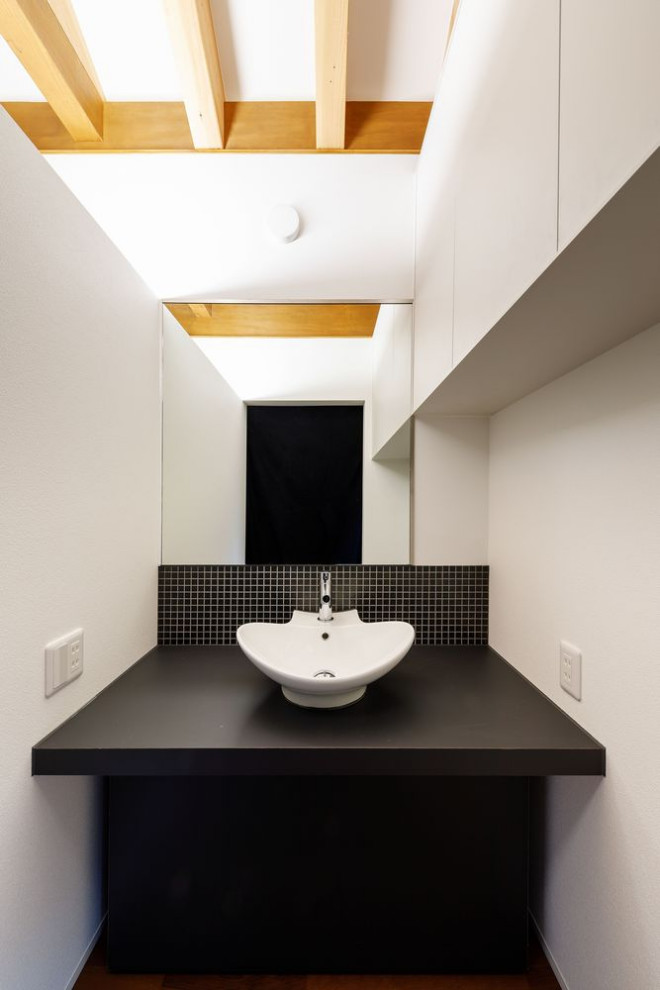 Inredning av ett modernt stort svart svart toalett, med släta luckor, svarta skåp, svart kakel, stenkakel, vita väggar, plywoodgolv, ett nedsänkt handfat, bänkskiva i akrylsten och brunt golv