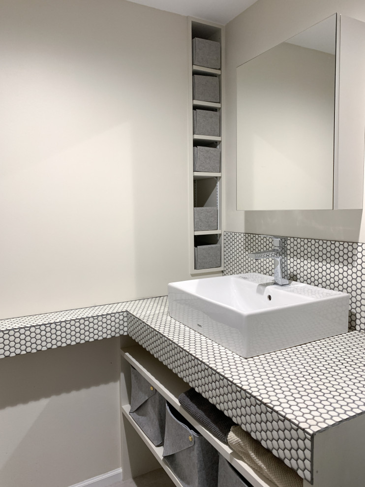 Aménagement d'un petit WC et toilettes moderne avec des portes de placard blanches, un mur beige, un sol en vinyl, une vasque, un plan de toilette en carrelage, un sol gris, un plan de toilette blanc et meuble-lavabo encastré.