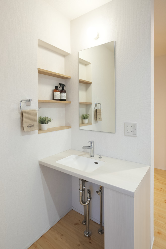 Esempio di un piccolo bagno di servizio industriale con pareti bianche, parquet chiaro, lavabo integrato e pavimento marrone