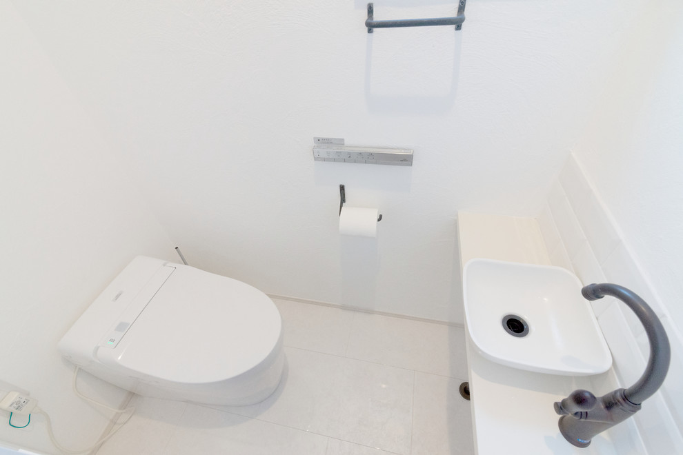 東京23区にあるモダンスタイルのおしゃれなトイレ・洗面所 (壁掛け式トイレ、白いタイル、白い壁、オーバーカウンターシンク、木製洗面台、白い床、白い洗面カウンター) の写真