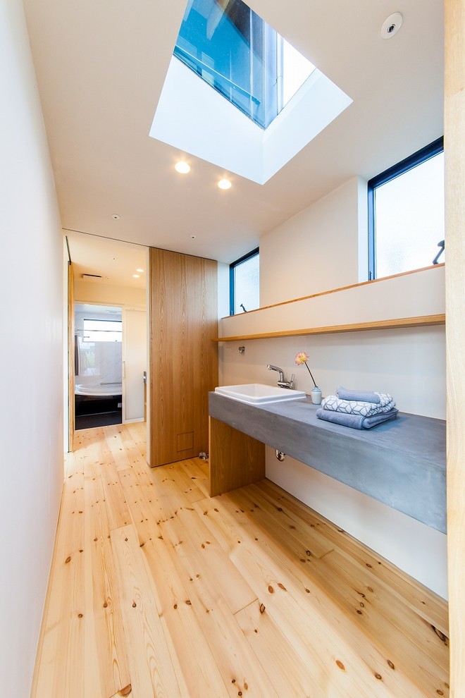 Modelo de aseo de estilo zen con paredes blancas, suelo de madera clara, lavabo encastrado, encimera de cemento y suelo beige