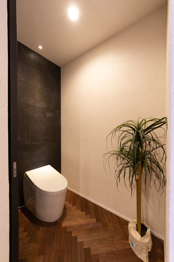 Exemple d'un WC et toilettes moderne avec un carrelage noir, des carreaux de béton, un mur noir, parquet foncé et un sol marron.