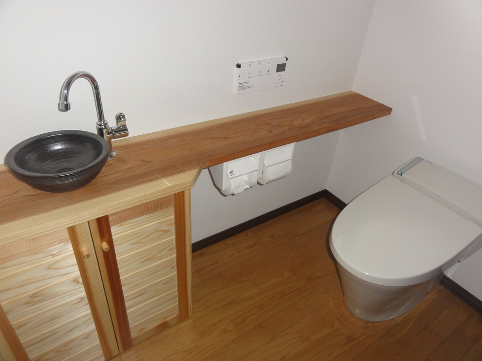 Cette image montre un grand WC et toilettes rustique en bois clair avec un placard en trompe-l'oeil, WC à poser, un mur blanc, parquet clair, un lavabo encastré et un sol beige.