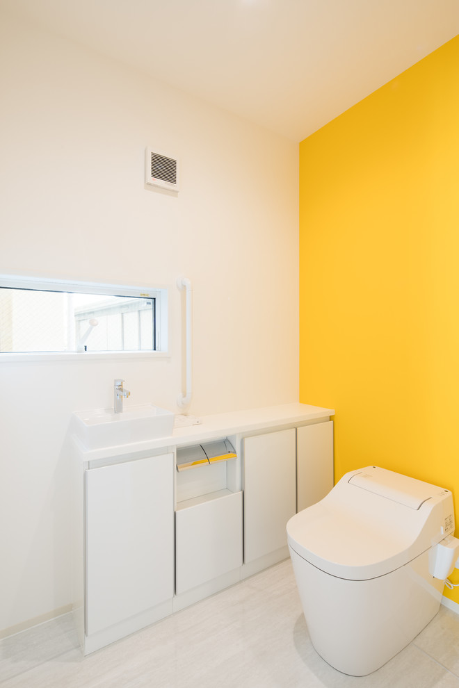 Moderne Gästetoilette mit flächenbündigen Schrankfronten, weißen Schränken, gelber Wandfarbe, Aufsatzwaschbecken, weißem Boden und weißer Waschtischplatte in Sonstige