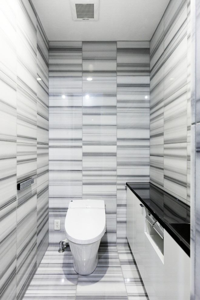 横浜にある中くらいなコンテンポラリースタイルのおしゃれなトイレ・洗面所 (黒いキャビネット、黒いタイル、大理石タイル、グレーの壁、大理石の床、人工大理石カウンター、グレーの床、白い洗面カウンター) の写真