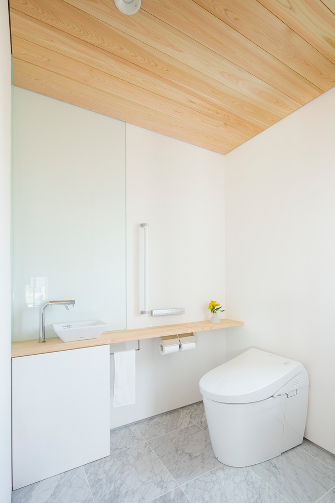 Aménagement d'un WC et toilettes moderne avec un mur blanc, une vasque, un plan de toilette en bois et un sol gris.