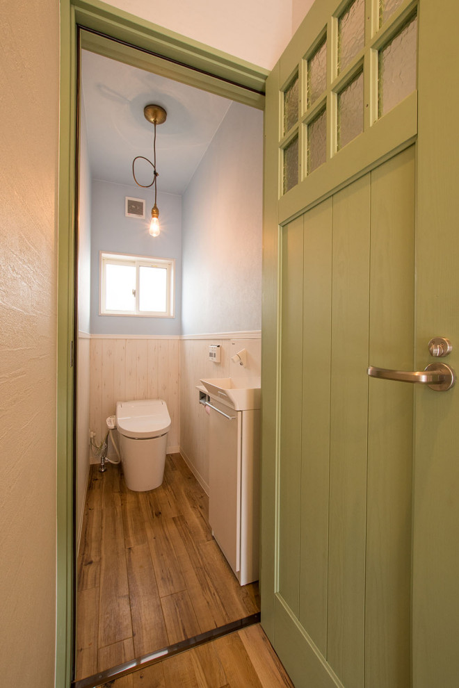 Cette image montre un petit WC et toilettes marin avec un placard en trompe-l'oeil, des portes de placard blanches, un mur bleu, un sol en vinyl, un sol marron, WC à poser, un lavabo suspendu, un plan de toilette en surface solide, un plan de toilette blanc, meuble-lavabo sur pied, un plafond en papier peint et du papier peint.
