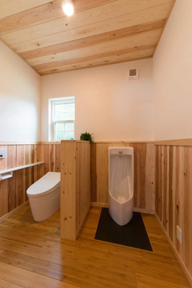 Idée de décoration pour un WC et toilettes craftsman avec un urinoir, un mur blanc et un sol en bois brun.