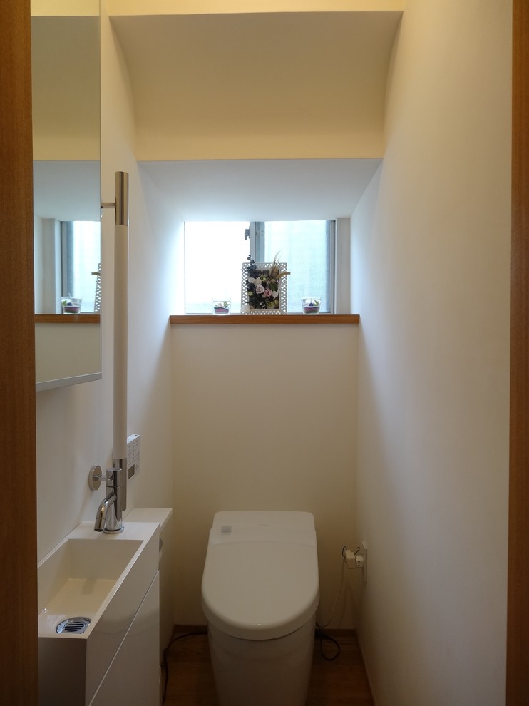 Exemple d'un grand WC et toilettes scandinave avec un placard à porte plane, des portes de placard blanches, WC à poser, un carrelage blanc, un sol en bois brun, un sol beige et un plan de toilette blanc.