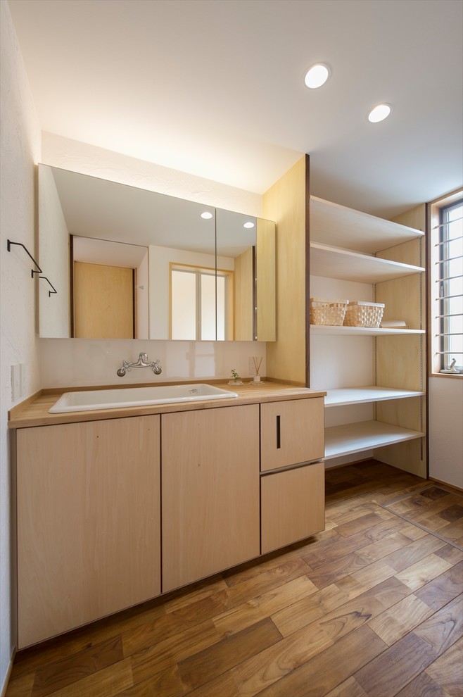 Inspiration for a world-inspired cloakroom in Other with flat-panel cabinets, light wood cabinets, white walls, medium hardwood flooring, a built-in sink, wooden worktops, brown floors and beige worktops.