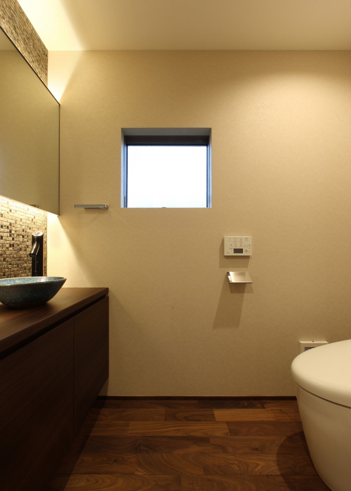 Foto på ett litet funkis brun toalett, med luckor med profilerade fronter, bruna skåp, beige kakel, mosaik, beige väggar, mörkt trägolv, ett fristående handfat, träbänkskiva och brunt golv