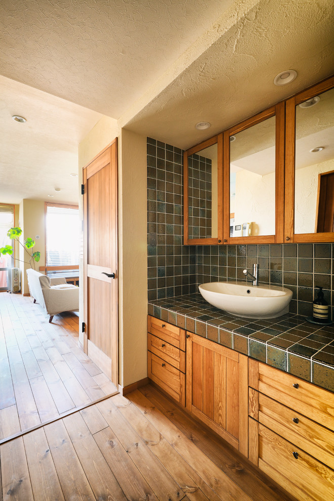 Inspiration for a world-inspired cloakroom in Other with recessed-panel cabinets, medium wood cabinets, beige walls, medium hardwood flooring, a vessel sink, tiled worktops and brown floors.