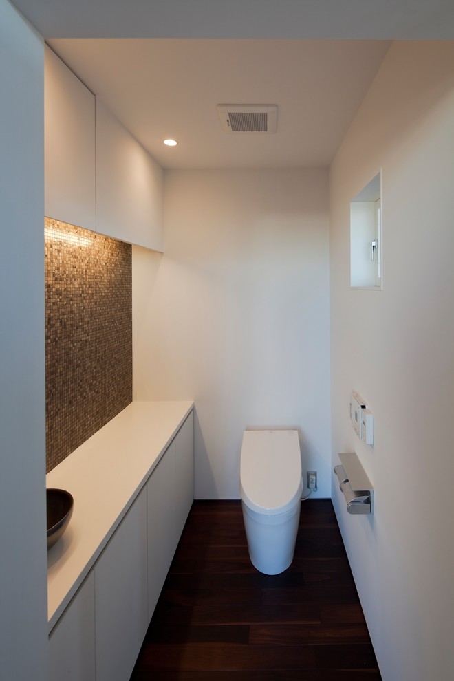 Источник вдохновения для домашнего уюта: большой туалет в стиле модернизм с плоскими фасадами, белыми фасадами, унитазом-моноблоком, коричневой плиткой, стеклянной плиткой и столешницей из искусственного камня
