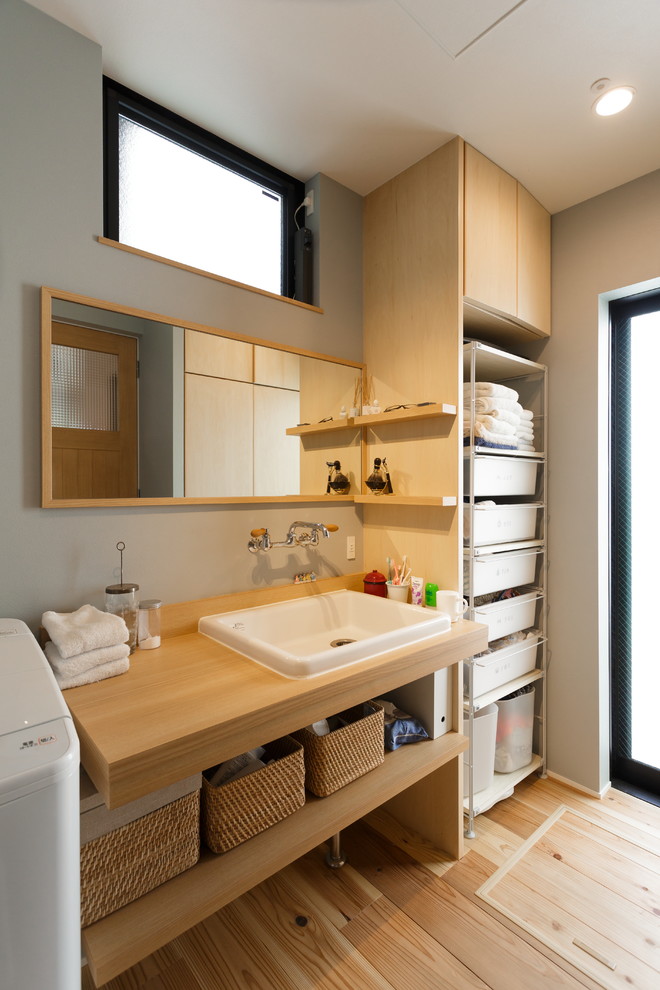 Пример оригинального дизайна: туалет в современном стиле с открытыми фасадами, серыми стенами, светлым паркетным полом, накладной раковиной, столешницей из дерева, бежевым полом и бежевой столешницей