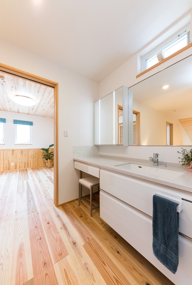 World-inspired cloakroom in Other with flat-panel cabinets, white cabinets, white walls, light hardwood flooring, beige floors and grey worktops.