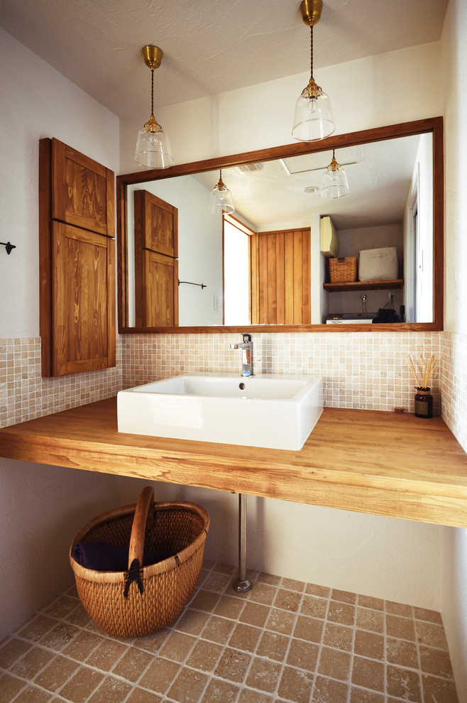 World-inspired cloakroom in Other with beige tiles, beige walls, a vessel sink, wooden worktops, brown floors and brown worktops.